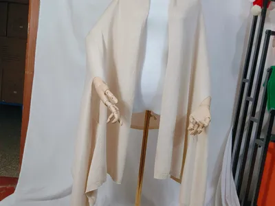 Cremefarbener Feinstrick-Wickelponcho mit offenem Vorderteil und geripptem Abschluss, locker auf einer Schneiderpuppe drapiert