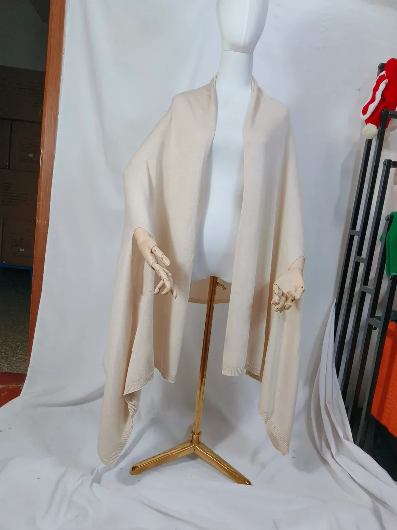 Cremefarbener Feinstrick-Wickelponcho mit offenem Vorderteil und geripptem Abschluss, locker auf einer Schneiderpuppe drapiert