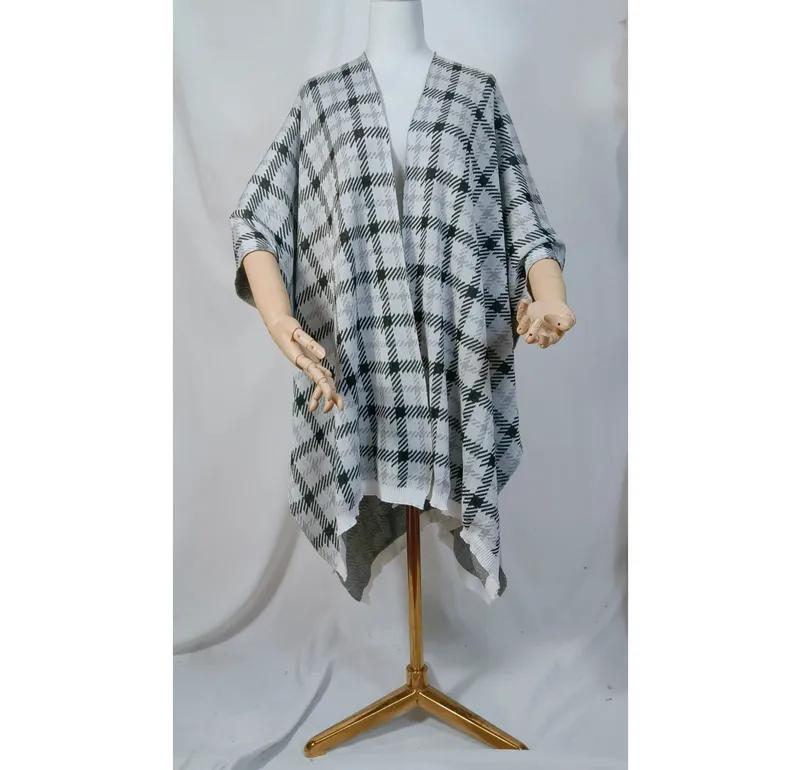 Schneiderpuppe mit schwarzem und weißem Karomuster-Strickponcho, offenem Vorderteil und asymmetrischem Saum auf goldenem Ständer