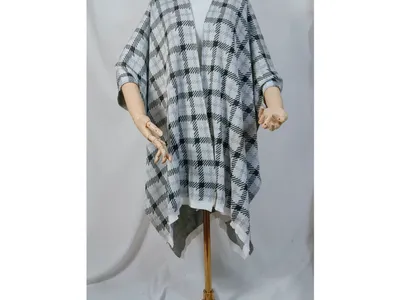 Schneiderpuppe mit schwarzem und weißem Karomuster-Strickponcho, offenem Vorderteil und asymmetrischem Saum auf goldenem Ständer