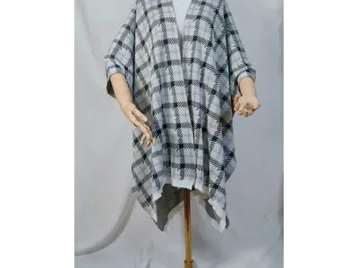 Schwarz-weißer Hahnentritt-Karo-Strickponcho mit offenem Vorderteil, drapiert auf einer Schneiderpuppe mit goldenem Ständer