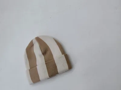 Kleine gestrickte Mütze mit breiten vertikalen Streifen in Beige und Creme, flach auf hellem Untergrund fotografiert