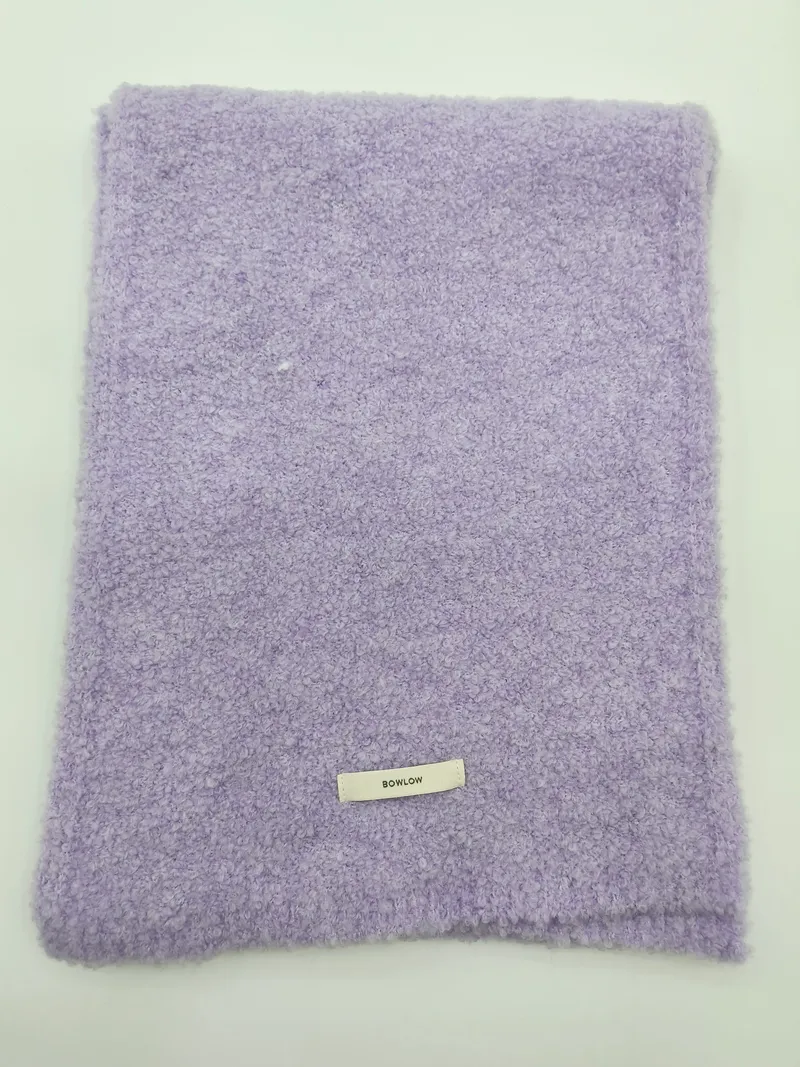 Gefaltete weiche Kuscheldecke in Fliederviolett mit Boucle-Oberfläche und kleinem Etikett auf weißem Hintergrund