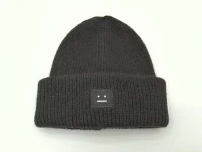 Schwarze Wintermütze in grobem Rippenstrick mit umgeschlagenem Bund und kleinem quadratischem besticktem Logo-Aufnäher auf weißem Hintergrund