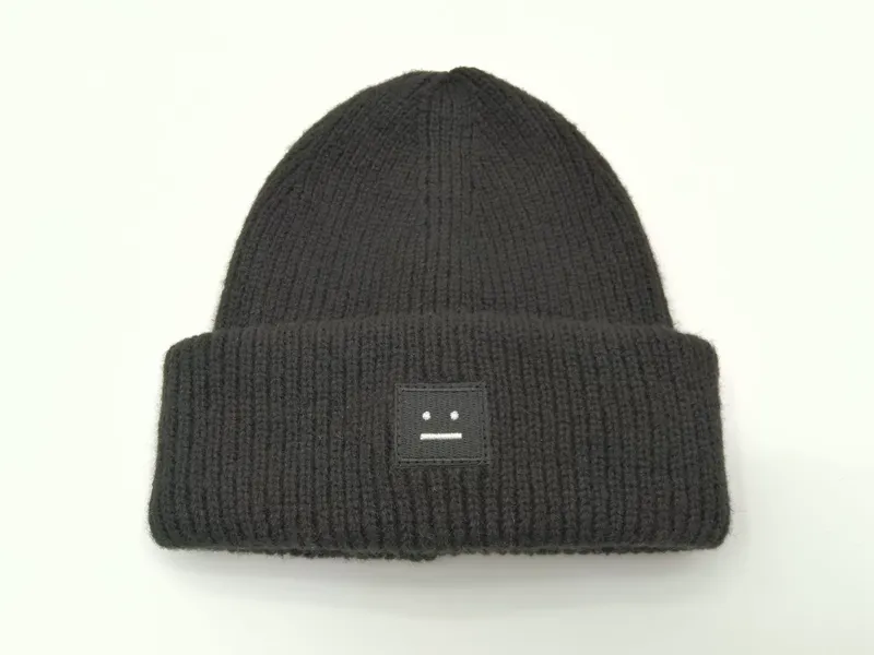 Schwarze Wintermütze in grobem Rippenstrick mit umgeschlagenem Bund und kleinem quadratischem besticktem Logo-Aufnäher auf weißem Hintergrund