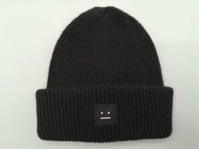 Schwarze fein gerippte Strickmütze mit umgeschlagenem Rand und kleinem besticktem Motiv-Patch auf weißem Hintergrund