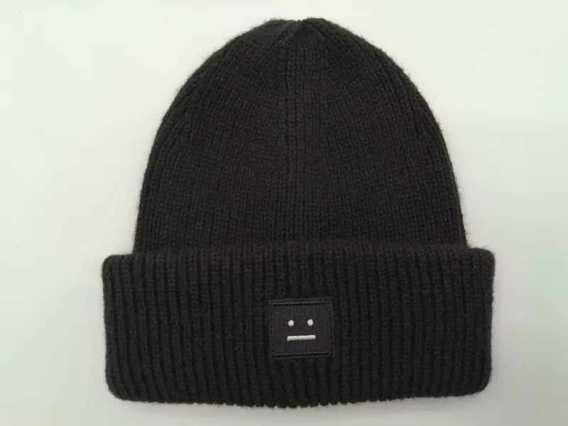 Schwarze fein gerippte Strickmütze mit umgeschlagenem Rand und kleinem besticktem Motiv-Patch auf weißem Hintergrund