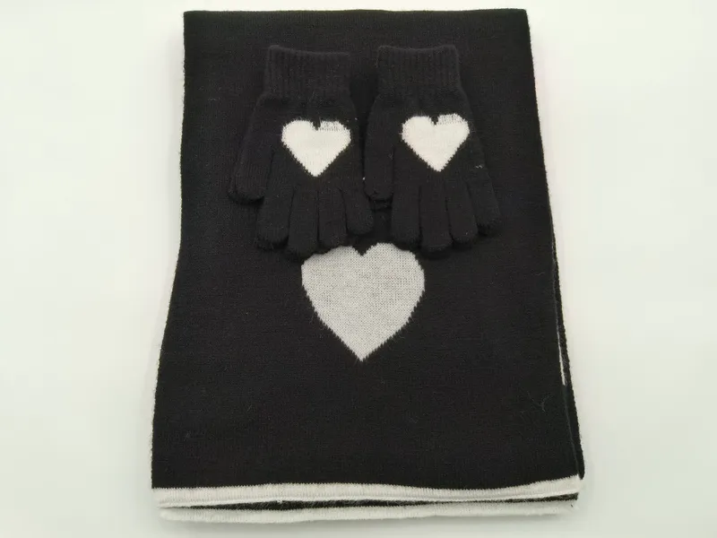 Schwarzes Strick-Set aus gefaltetem Schal und Handschuhen mit weißem Intarsia-Herzmuster auf weißem Hintergrund