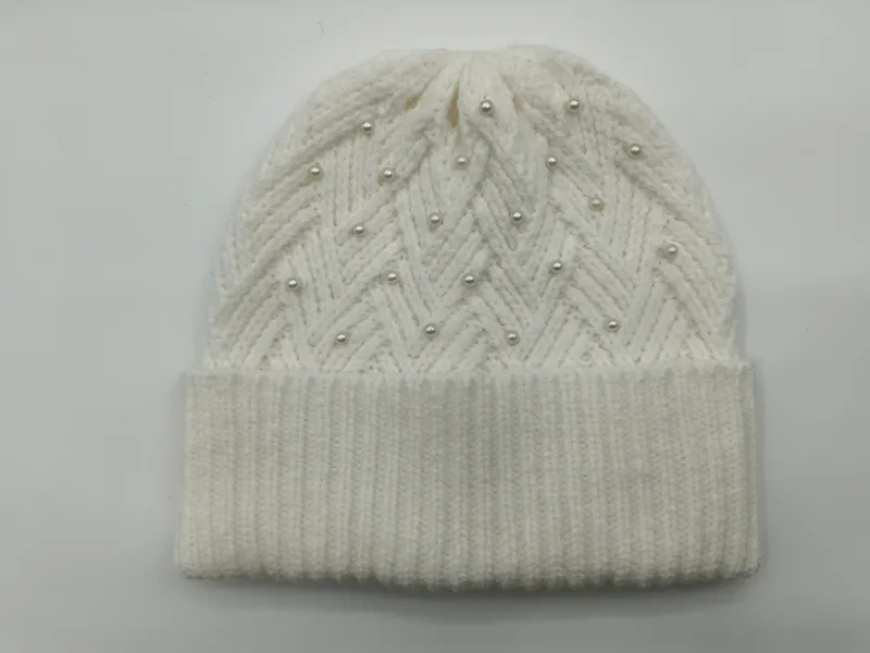Cremeweiße grob gestrickte Beanie mit Zickzack-Chevron-Muster und aufgesetzten Perlenapplikationen auf grauem Hintergrund