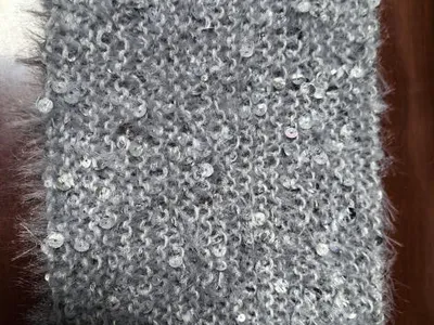 Nahaufnahme eines grauen Flauschstoffmusters mit vereinzelten Silberpailletten auf Holzuntergrund