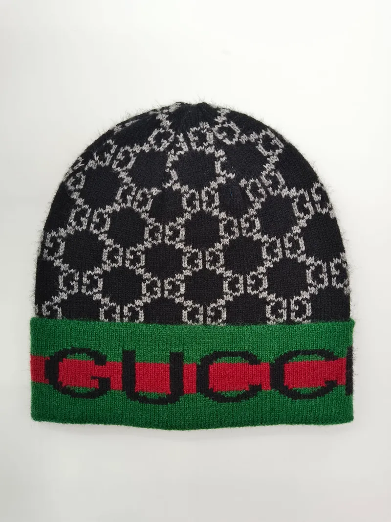 Schwarz-graue Strickmütze mit ineinandergreifendem Monogramm-Jacquard-Muster und grün-rot gestreiftem Rippenabschluss auf weißem Hintergrund