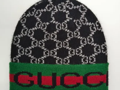 Schwarz-graue Strickmütze mit ineinandergreifendem Monogramm-Jacquard-Muster und grün-rot gestreiftem Rippenabschluss auf weißem Hintergrund