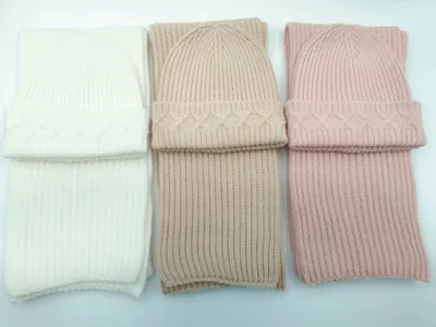 Drei aufeinander abgestimmte Zopfstrick-Beanie und Rippschal Sets in Elfenbein, Taupe und Altrosa nebeneinander auf weißem Hintergrund