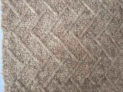 Nahaufnahme einer beigefarbenen Wollmisch-Wurfdecke mit Rautengitterstrickmuster und geripptem Rand