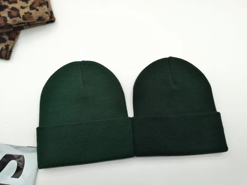 Zwei dunkelgrüne Strickmützen mit Umschlagrand in satterem Waldgrün, nebeneinander auf weißem Untergrund neben Leopardenstoff