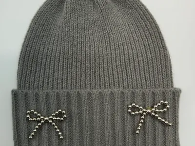 Graue Wintermütze mit Umschlagrand und zwei silbernen Perlen-Schleifenbroschen auf weißem Hintergrund in Draufsicht