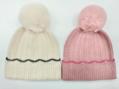 Zwei Strickbommelmützen nebeneinander – eine cremefarben mit schwarzem Glitzerrand und eine rosa mit rosafarbenem Glitzerrand, beide mit Kunstfellbommel