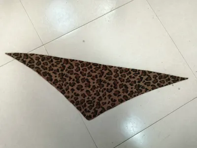 Dreieckiges Halstuch mit braunem Leoparden-Cheetah-Muster flach auf weißem Fliesenboden ausgebreitet