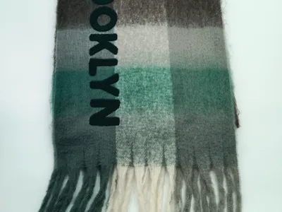 Gefalteter Karoschal in Grün, Grau und Creme mit Brooklyn-Stickerei und Fransenenden auf weißem Hintergrund