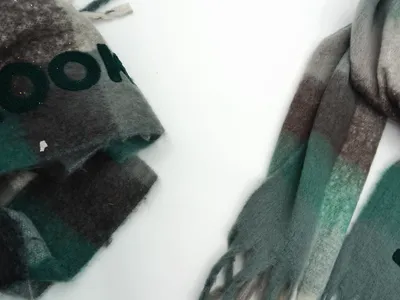 Zwei Karostoffe aus Wollmischung in Grün-Grau-Braun-Ombré mit Fransenenden, einer gefaltet und einer ausgebreitet auf weißem Untergrund