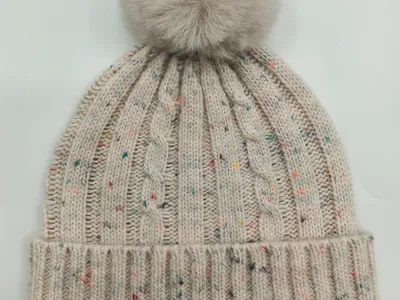 Cremefarbene Zopfstrickmütze mit bunten Farbsprenkeln und großem flauschigem Kunstfell-Bommel auf der Spitze