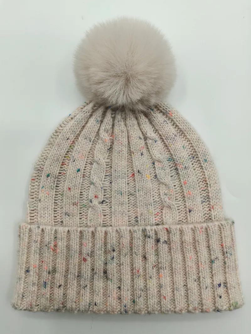 Cremefarbene Zopfstrickmütze mit bunten Farbsprenkeln und großem flauschigem Kunstfell-Bommel auf der Spitze