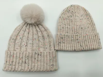 Zwei cremefarbene Strickmützen mit Farbsprenkeln nebeneinander – Zopfstrickvariante mit Kunstfell-Bommel und Rippenstrickvariante mit Umschlagrand
