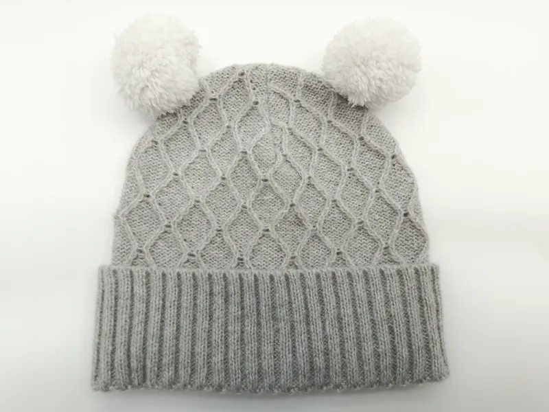 Hellgraue Strickmütze für Babys mit zwei flauschigen Pompons und Umschlagbündchen, Detailaufnahme auf hellem Untergrund