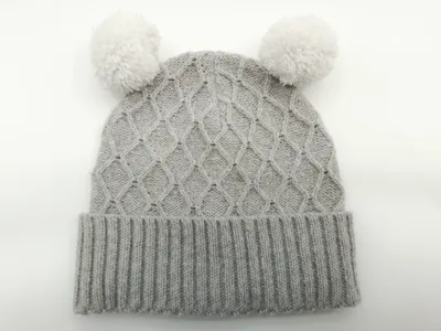 Hellgraue Strickmütze für Babys mit zwei flauschigen Pompons und Umschlagbündchen, Detailaufnahme auf hellem Untergrund