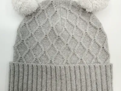 Strukturierte Wintermütze in Grau mit doppeltem weißem Bommel und breitem Strickbündchen, von oben fotografiert auf weißem Hintergrund