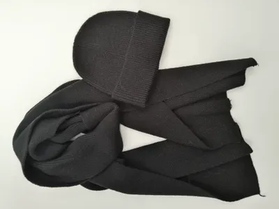 Schwarze gerippte Strickmütze mit dazu passendem langen Strickschal, flach auf weißem Hintergrund liegend, Materialstruktur sichtbar