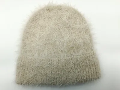 Beige-cremefarbene Mütze aus Eyelash-Garn mit flauschiger Fadenstruktur und Rippbündchen auf weißem Hintergrund