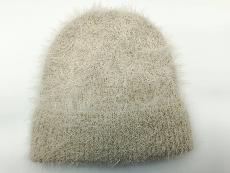 Beige-cremefarbene Mütze aus Eyelash-Garn mit flauschiger Fadenstruktur und Rippbündchen auf weißem Hintergrund