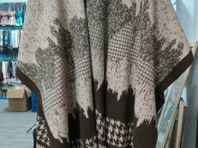 Großer Strickponcho in Beige und Braun mit Blattmotiv-Jacquard, Hahnentritt-Bordüre und Fransensaum auf einem Kleiderbügel