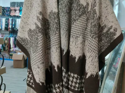 Offener Strickponcho in Beige und Braun mit floralem Jacquardmuster, Hahnentritt-Bordüre und Fransenabschluss auf Bügel
