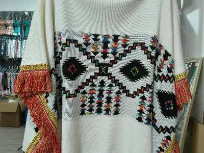 Cremefarbener Oversize-Rollkragenponcho mit buntem geometrischem Aztekenmuster und roten Fransen an den Ärmeln auf Schneiderpuppe