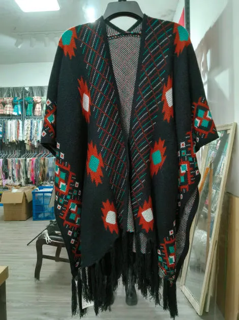 Offener schwarzer Strickponcho mit petrol-, rost- und weißfarbenem Aztekenmuster sowie Fransen am Saum auf Kleiderbügel