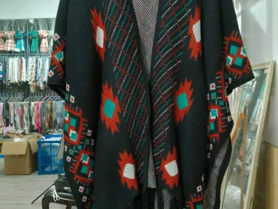 Offener schwarzer Strickponcho mit petrol-, rost- und weißfarbenem Aztekenmuster sowie Fransen am Saum auf Kleiderbügel