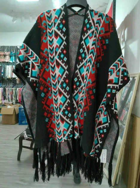 Offener schwarzer Strickponcho mit rot-petrol-weißem Aztekenmuster und Fransen am Saum auf Kleiderbügel