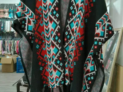 Offener schwarzer Strickponcho mit rot-petrol-weißem Aztekenmuster und Fransen am Saum auf Kleiderbügel