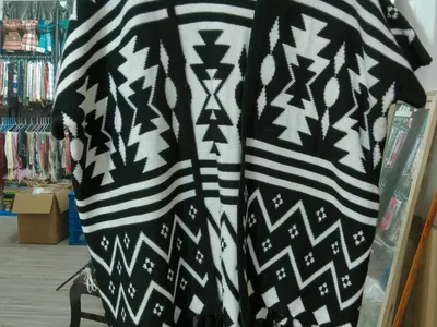 Strickponcho in Schwarz und Weiß mit geometrischem Aztekenmuster und Quastenfransenabschluss auf Kleiderbügel