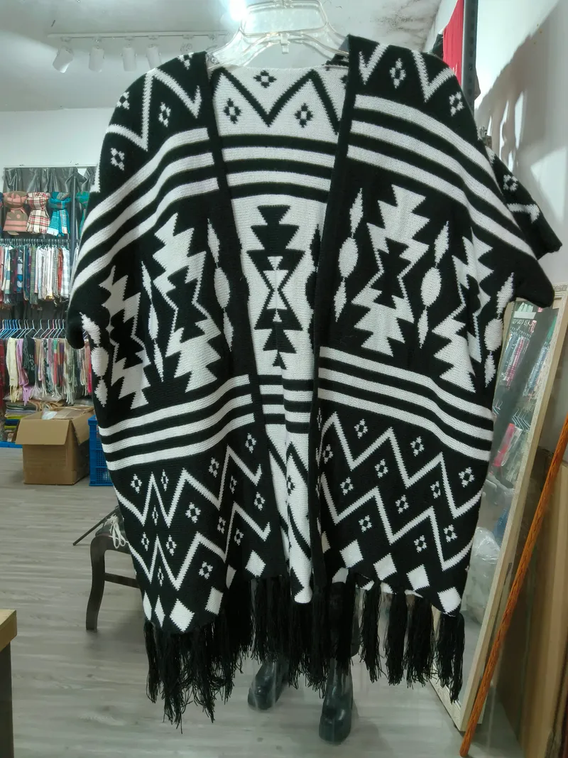 Strickponcho in Schwarz und Weiß mit geometrischem Aztekenmuster und Quastenfransenabschluss auf Kleiderbügel