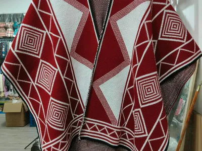 Strickponcho in Rot und Weiß mit auffälligem geometrischem Diamant- und Rautenmuster auf Kleiderbügel in einem Geschäft