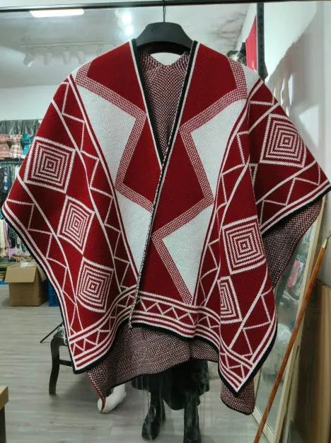 Strickponcho in Rot und Weiß mit auffälligem geometrischem Diamant- und Rautenmuster auf Kleiderbügel in einem Geschäft