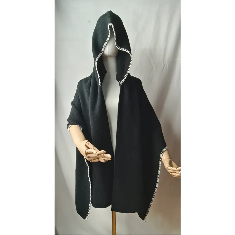 Eleganter schwarzer Kapuzenponcho aus Wolle mit kunstvollem weißem Bordürenmuster auf Schneiderpuppe mit Holzhänden