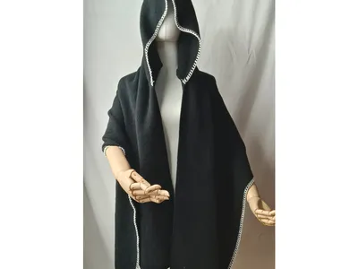Eleganter schwarzer Kapuzenponcho aus Wolle mit kunstvollem weißem Bordürenmuster auf Schneiderpuppe mit Holzhänden