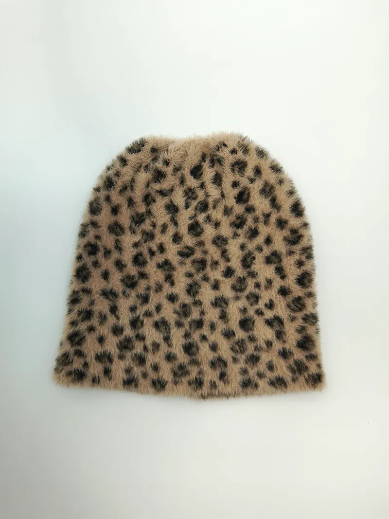 Draufsicht auf eine flauschige Strickmütze mit Leopardenmuster in Sandtönen und dunklen Flecken auf weißem Untergrund