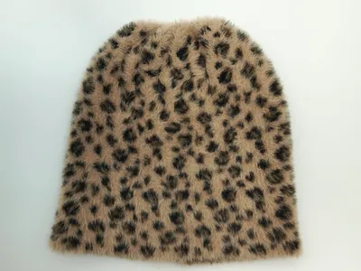Draufsicht auf eine flauschige Strickmütze mit Leopardenmuster in Sandtönen und dunklen Flecken auf weißem Untergrund