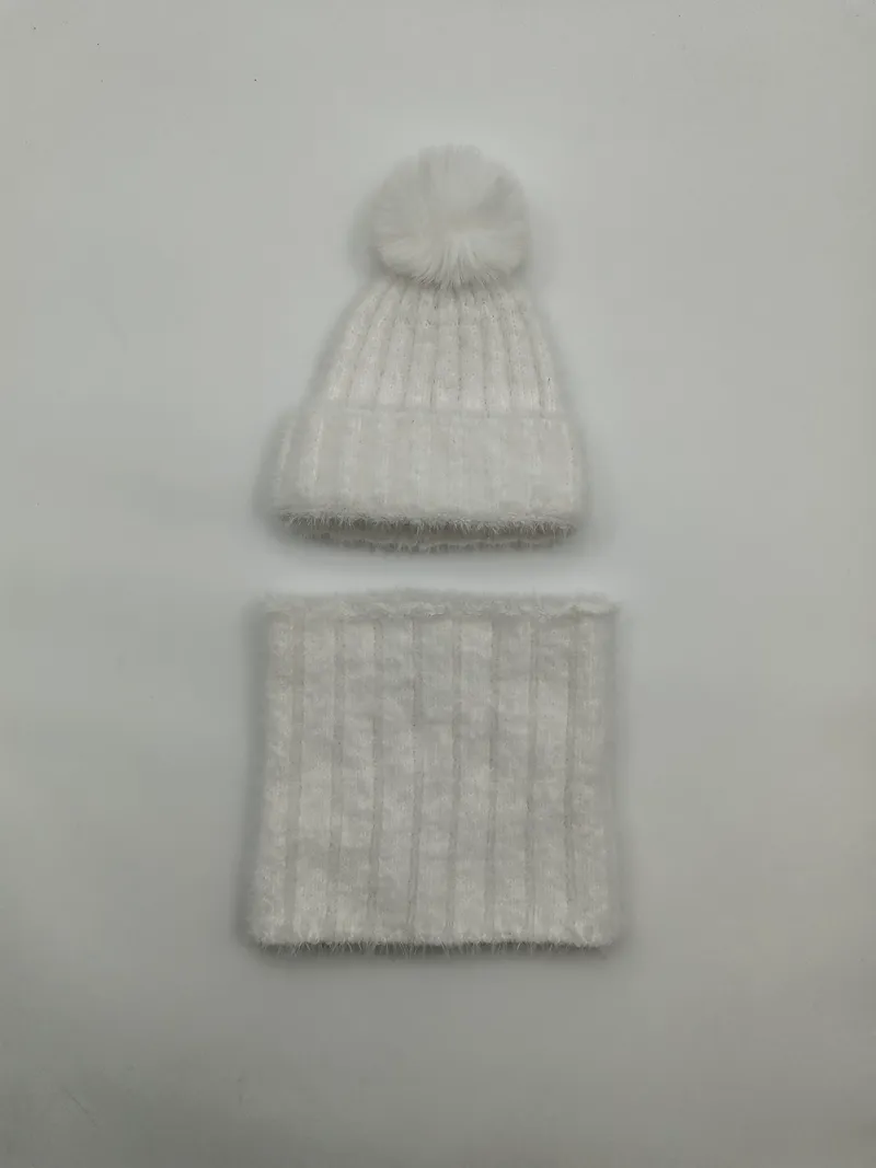 Weißes flauschiges Rippenstrick-Winterset mit Kunstfellbommel-Beanie und passendem Halsschlauch auf grauem Hintergrund
