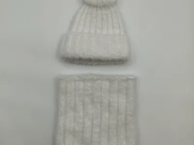 Weißes flauschiges Rippenstrick-Winterset mit Kunstfellbommel-Beanie und passendem Halsschlauch auf grauem Hintergrund